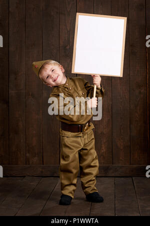 Bambini Bambino sono vestita come soldato rétro uniformi militari. Egli detiene il poster in bianco per i veterani ritratto. Foto Stock