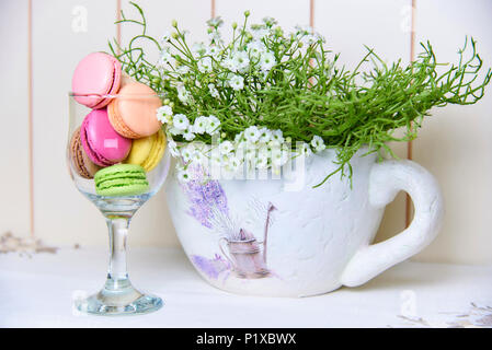 Luminose biscotti colorati in un bicchiere vicino a un bel vaso decorativo con fiori. Foto Stock