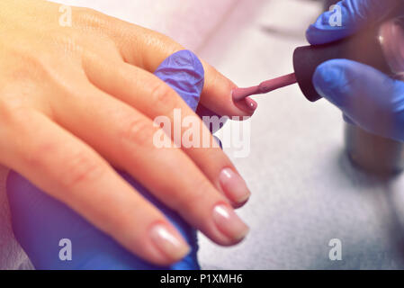 La cura delle unghie e manicure. Primo piano della bella Mani femminili trasparente applicazione di smalto per unghie su sano e naturale della donna di chiodi in un salone di bellezza. Manicuris Foto Stock