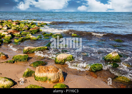 Le onde rompono su una grande pietra su nuvoloso giorno di estate Foto Stock