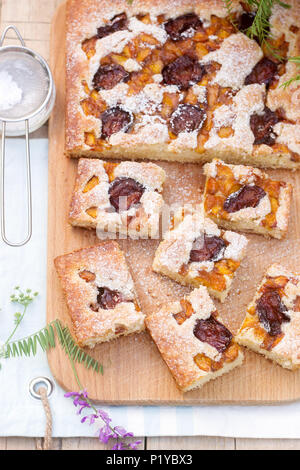 Pezzi di torta di frutta con pezzi di prugne e di pesche e un mazzo di fiori su un tavolo di legno. In stile rustico, il fuoco selettivo. Foto Stock