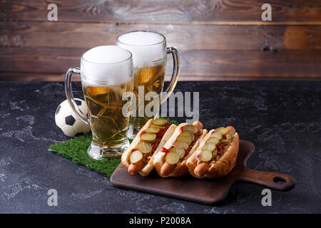 Foto di due bicchieri di birra, hot dogs, pallone da calcio Foto Stock