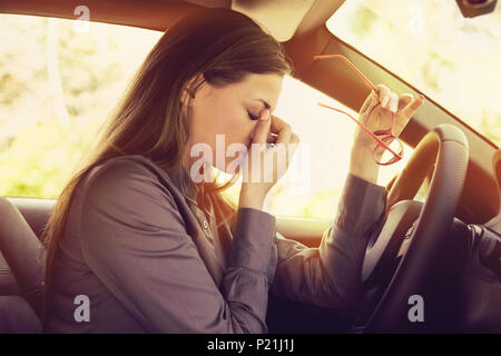 Business donna avente mal di testa tenendo fuori la sua gli occhiali ha per fare una sosta dopo una guida auto nel traffico in ora di punta. Esaurito, oberati di lavoro autista c Foto Stock