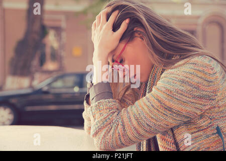 Profilo laterale ha sottolineato triste giovane donna seduti all'aperto con ripartiti in auto in background. Città urban life style lo stress Foto Stock