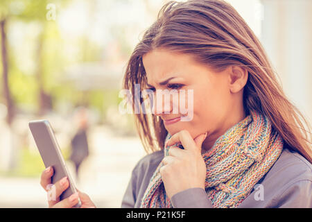 Closeup ritratto triste e scettico, infelice, donna texting sul telefono orinato con conversazione isolato sfondo all'aperto. Negativo emozione umana faci Foto Stock