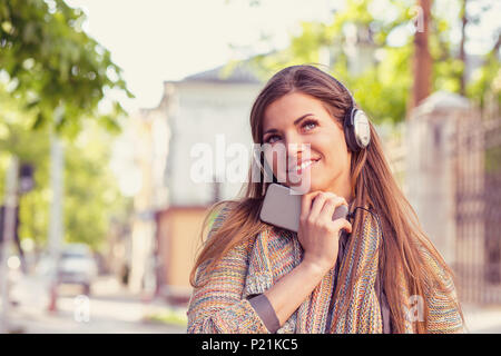 Bella donna fantasticando ascoltando la musica su un telefono intelligente a piedi giù per la strada a un autunno giornata di sole Foto Stock