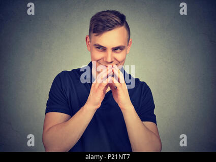 Subdolo uomo tramando qualcosa isolato sul muro grigio Sfondo. Negativo emozione umana espressione facciale sensazione atteggiamento Foto Stock