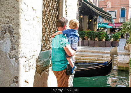 Padre porta ragazzo giovane come guardare la gondola e passate a Venezia in Italia. Venezia può essere un ottimo posto da visitare con i bambini e neonati. Foto Stock