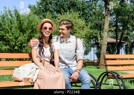 Giovane coppia multietnica in appoggio sul banco in park insieme Foto Stock