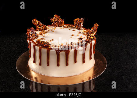 Bianco rotondo torta con caramello e cioccolato riso soffiato su un vassoio rotondo su sfondo nero Foto Stock