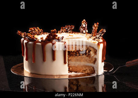 Bianco rotondo torta con caramello e cioccolato riso soffiato su un vassoio rotondo su sfondo nero Foto Stock