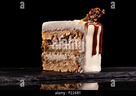 Pezzo di torta bianca con caramello e cioccolato riso soffiato su un vassoio nero su sfondo nero Foto Stock