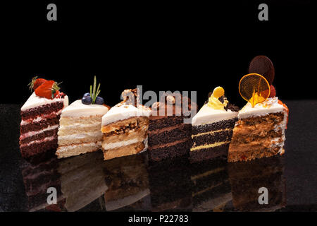 Un assortimento di grandi pezzi di diverse torte: cioccolato, lamponi, fragole, i dadi, i mirtilli. Pezzi di torte su una tavola nera. Foto Stock