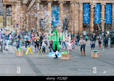 Maschio intrattenitore Street di Edimburgo vestito in un costume colorato divertente adulti e bambini facendo un sacco di bolle di sapone galleggiante nel cielo. Foto Stock