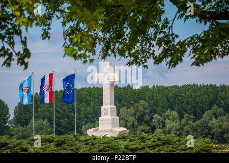 Una vista della croce un monumento che dice alle vittime di guerra per libero Croazia in memoria di guerra croato difensori con bandiere issate accanto a Vukovar Foto Stock