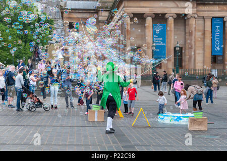 Maschio intrattenitore Street di Edimburgo vestito in un costume colorato divertente adulti e bambini facendo un sacco di bolle di sapone galleggiante nel cielo. Foto Stock