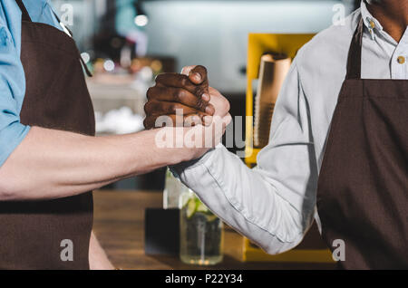 Ritagliato colpo di due proprietari di coffee shop in grembiuli stringono le mani in un coffee shop Foto Stock