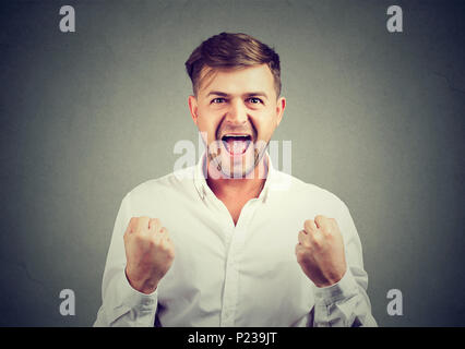 Bello allegro Uomo in camicia bianca tenendo i pugni fino super eccitati con nuovo successo. Foto Stock