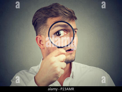 Giovane uomo espressiva cercando scioccati mentre guardando la telecamera attraverso la lente di ingrandimento. Foto Stock