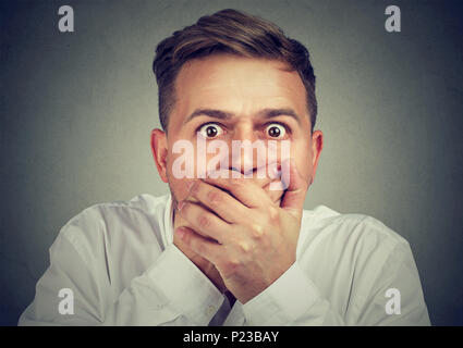 Ritratto di giovane uomo che copre la bocca con entrambe le mani nella paura cercando espressamente alla fotocamera. Foto Stock