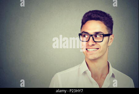 Sorridente uomo curioso guardando dal lato isolato su sfondo grigio con copia spazio. Le emozioni umane Foto Stock