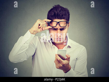 Giovane Uomo con occhiali aventi problemi a visualizzare cellulare ha problemi di visione. Bad messaggio di testo. Human percezione dell emozione Foto Stock