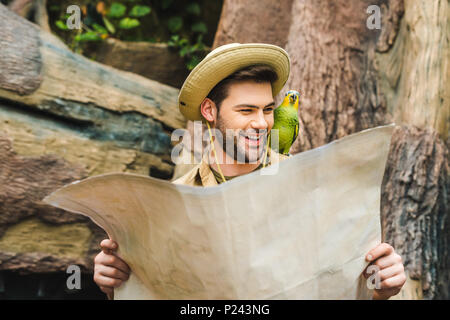 Felice giovane con pappagallo sulla spalla e mappa nella giungla Foto Stock