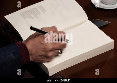 Man mano con penna che scrive sul libro. Foto Stock