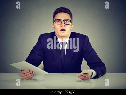 Occupato dipendente confuso con lo smartphone e tablet pc Foto Stock
