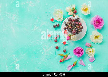 Tazza di erbe di bacche di ciliegio,rosa tea con mazzo di rose di diramazione ,olio essenziale. Le piante officinali e aromatiche composizione. Piano di composizione dei laici con deliziosi frutti di bosco. Spazio di copia Foto Stock