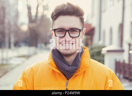 Bel giovane studente in abbigliamento esterno e occhiali sorridente alla fotocamera su sfondo di street. Foto Stock