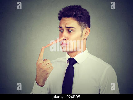 Preoccupato per il business man con il naso lungo isolato sul muro grigio Sfondo. Concetto bugiardo. Foto Stock