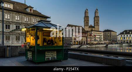 Tipiche bancarelle di vendita di castagne sulla Rathausbrücke (ponte) a Zurigo in serata, Limmatquai e Frauenmünster chiesa in background Foto Stock