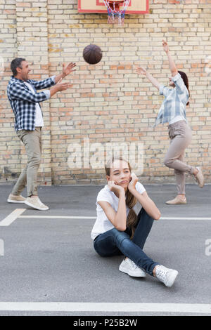 Sconvolto figlia con genitori felici giocare a basket dietro Foto Stock