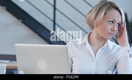 Stanco giovane donna nel lavoro di ufficio con un computer portatile e a fissare lo schermo del computer Foto Stock