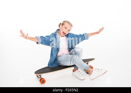 Bambino eccitato in denim oversize shirt seduti su un longboard, isolato su bianco Foto Stock