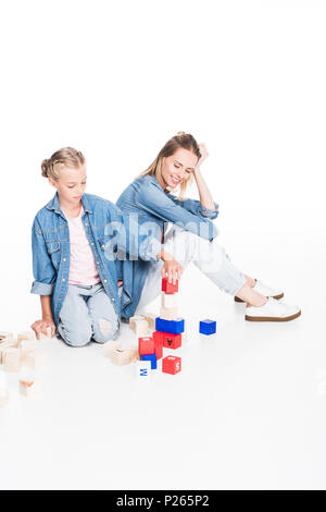 Piccola figlia lettera di impilamento cubetti in una torre e sua madre seduta accanto a lei, isolato su bianco Foto Stock