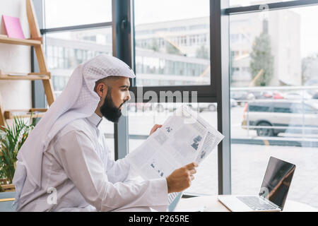 Bel giovane imprenditore musulmano leggendo il giornale in ufficio moderno Foto Stock