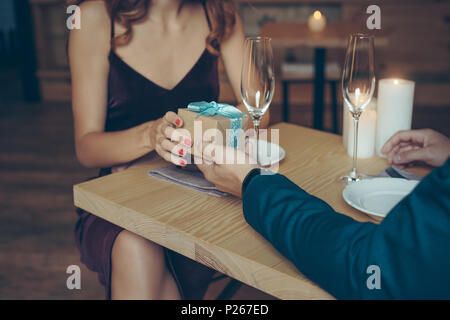 Ritagliato shot della giovane azienda avvolto confezione regalo durante una cena romantica nel ristorante Foto Stock