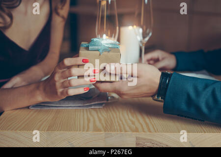Ritagliato shot della giovane azienda avvolto confezione regalo durante una cena romantica nel ristorante Foto Stock