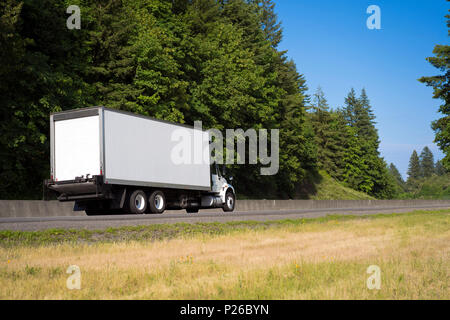 Commercial big rig giorno cabina raggio locale white semi carrello trasporto dry van rimorchio della scatola sul verde highway road con alberi per la consegna di industria Foto Stock