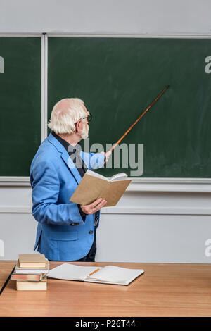 Capelli grigi professore azienda prenota e puntando su qualcosa di Blackboard Foto Stock