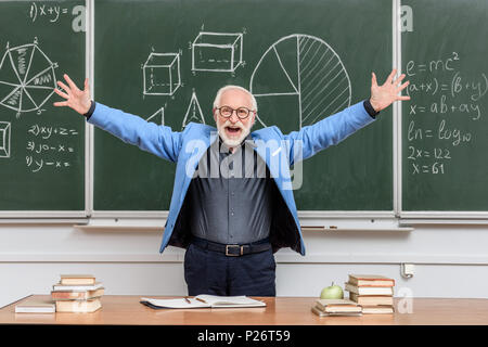 Felice senior lecturer a braccia aperte in piedi vicino a lavagna Foto Stock