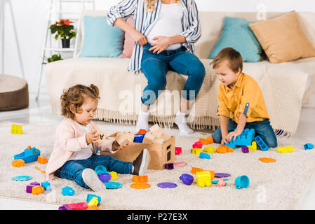 Ritagliato shot della donna incinta seduta sul divano e ci sono bambini che giocano con i blocchi colorati a casa Foto Stock