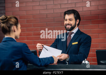 Hotel receptionist che mostra contratto il cliente al bancone Foto Stock