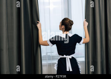 Vista posteriore del giovane bella cameriera in uniforme tende di chiusura Foto Stock