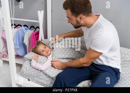 Padre di copertura poco adorabile figlia con coperta in letto Foto Stock