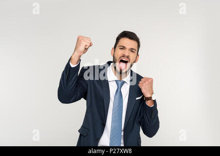 Eccitato giovane impreditore agitando i pugni e urlando in telecamera isolato su grigio Foto Stock