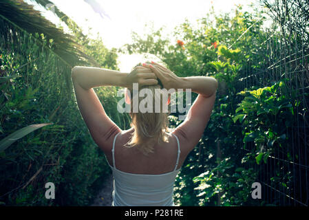 Vista posteriore della donna bionda che si immerse in qualche raggio per la vitamina D in un giardino sontuoso vicino a Punta del Este, Uruguay. Foto Stock