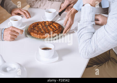 Immagine ritagliata della donna torta di taglio sul tavolo mentre gli amici seduti Foto Stock